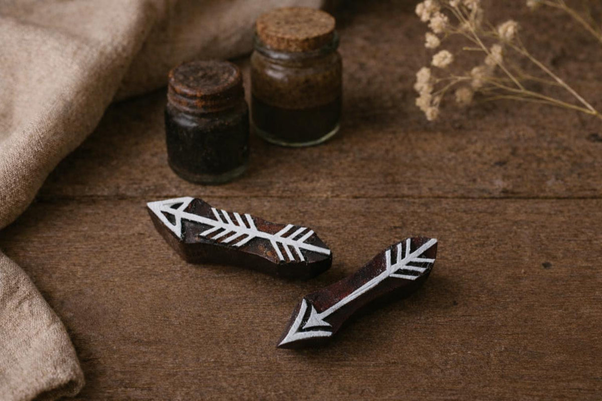 Two hand-carved wooden arrow stamps with minimalist tribal design placed on a rustic wooden table.