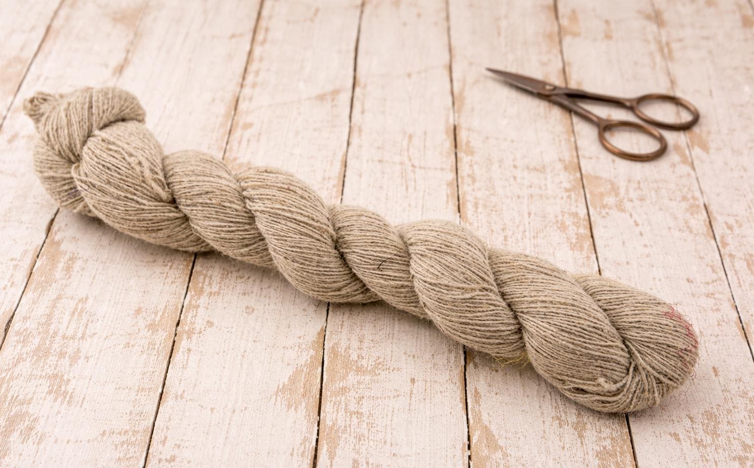 Machine spun hemp yarn skein blended with wool on rustic wooden surface with scissors