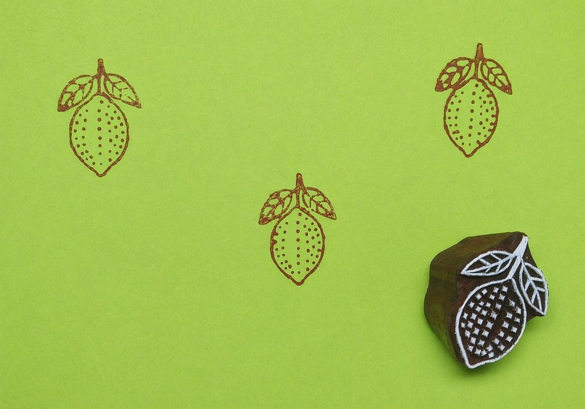 Lemon wooden printing block creating repeating fruit pattern on green background