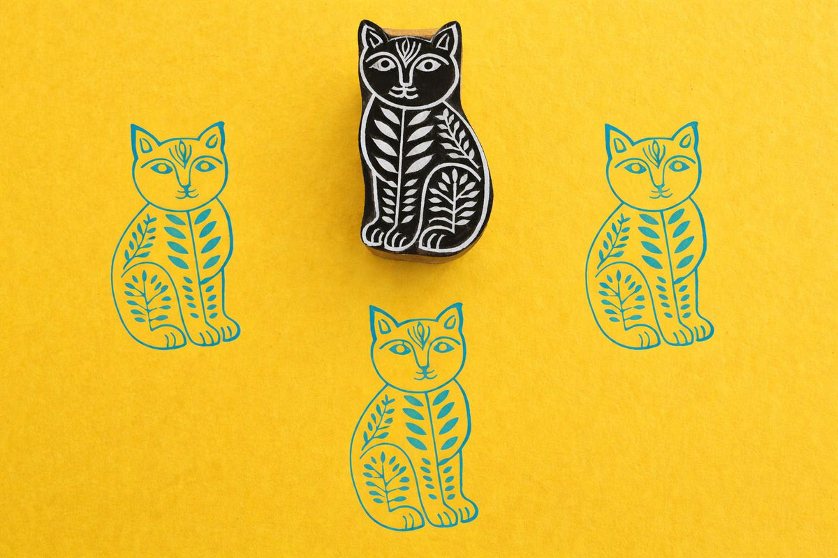 Hand carved wooden stamp of a stylised cat with leaf motifs printed in blue ink on yellow paper