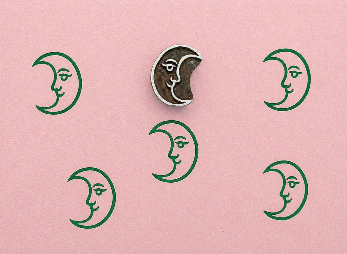 Crescent moon wooden stamp with repeating green moon prints on textured pink paper