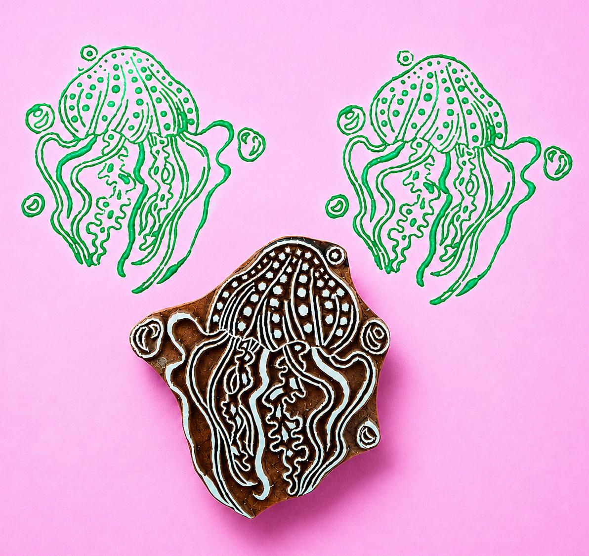 Hand carved Indian wooden block featuring a large jellyfish illustration printed in green on pink background for textile printing, pottery, clay, and ocean themed crafts.
