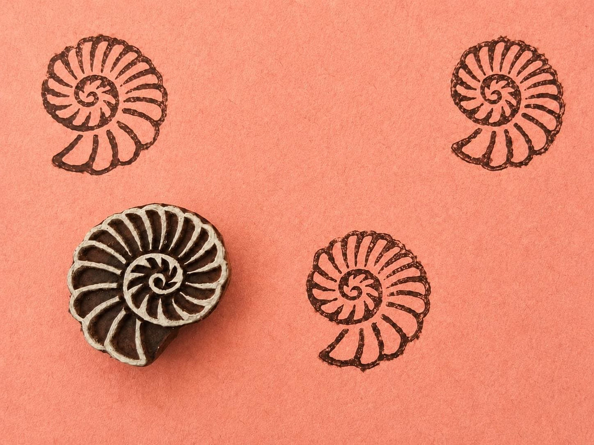 Hand carved wooden printing block featuring a coral fossil spiral shell motif stamped repeatedly on peach paper.