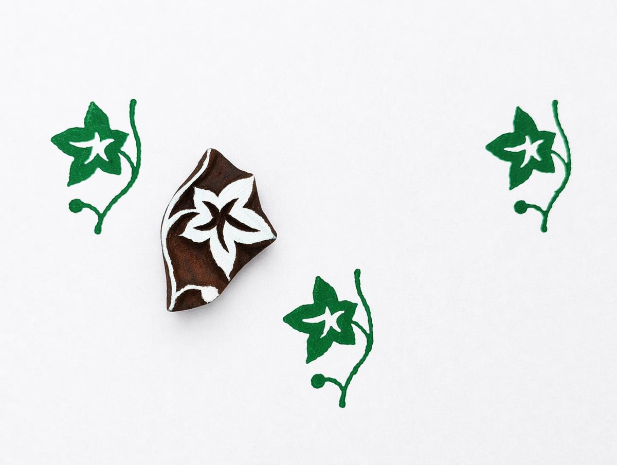 Hand carved wooden ivy vine block stamp printing small climbing leaf motif in green ink on white background