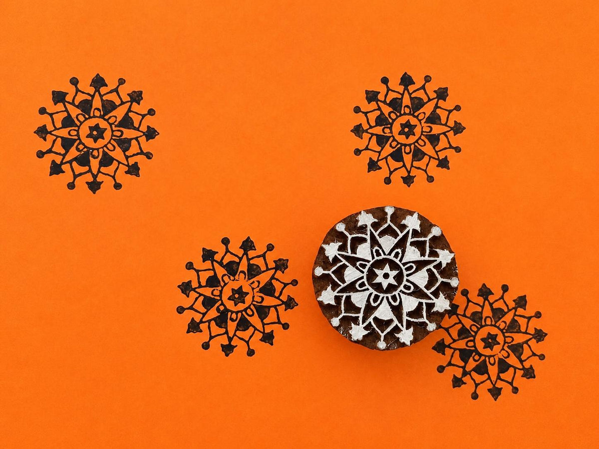 Hand carved wooden rosette compass block stamp printing intricate radial folk motif in black ink on orange background