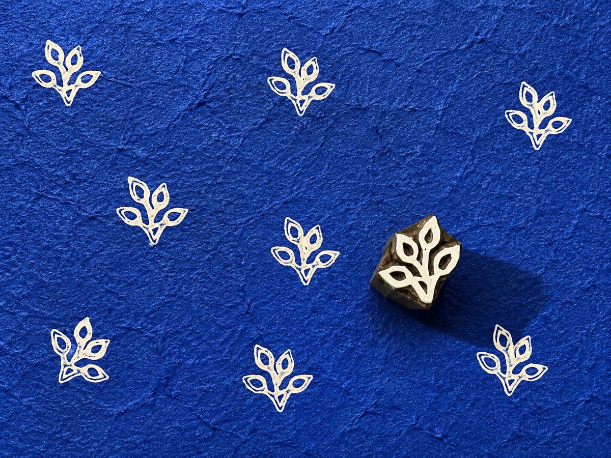 Tiny hand carved folk leaf wooden printing block stamped in white ink on textured cobalt blue handmade paper for fabric printing and paper crafts.