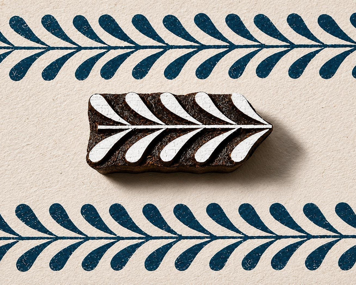 Hand carved wooden border block stamp printing repeating leafy vine border in deep blue ink on textured handmade paper
