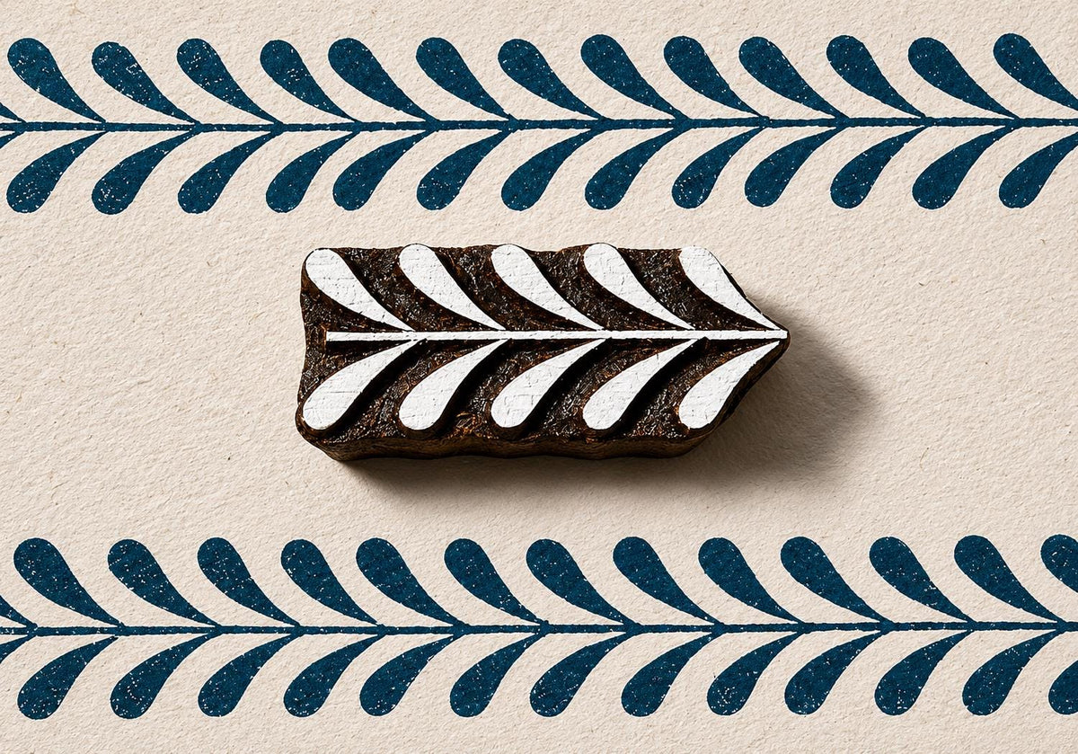 Hand carved wooden border block stamp printing repeating leafy vine border in deep blue ink on textured handmade paper