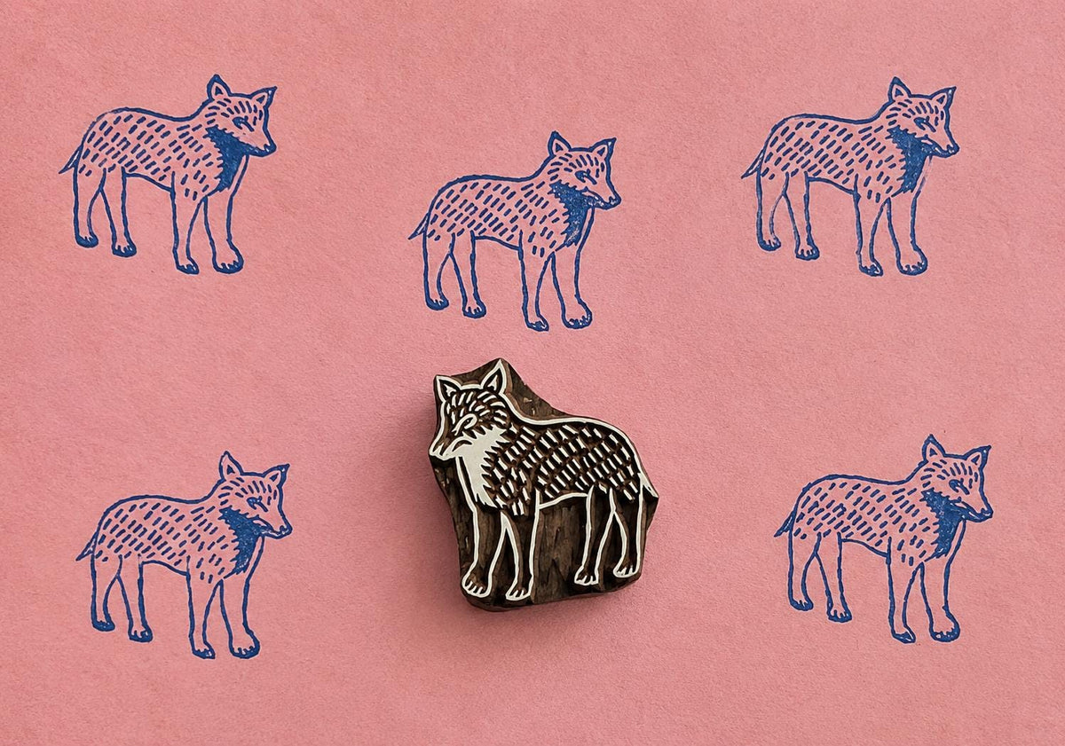 Hand carved Watchful Wolf wooden block stamp with repeated wolf prints on pink handmade paper.
