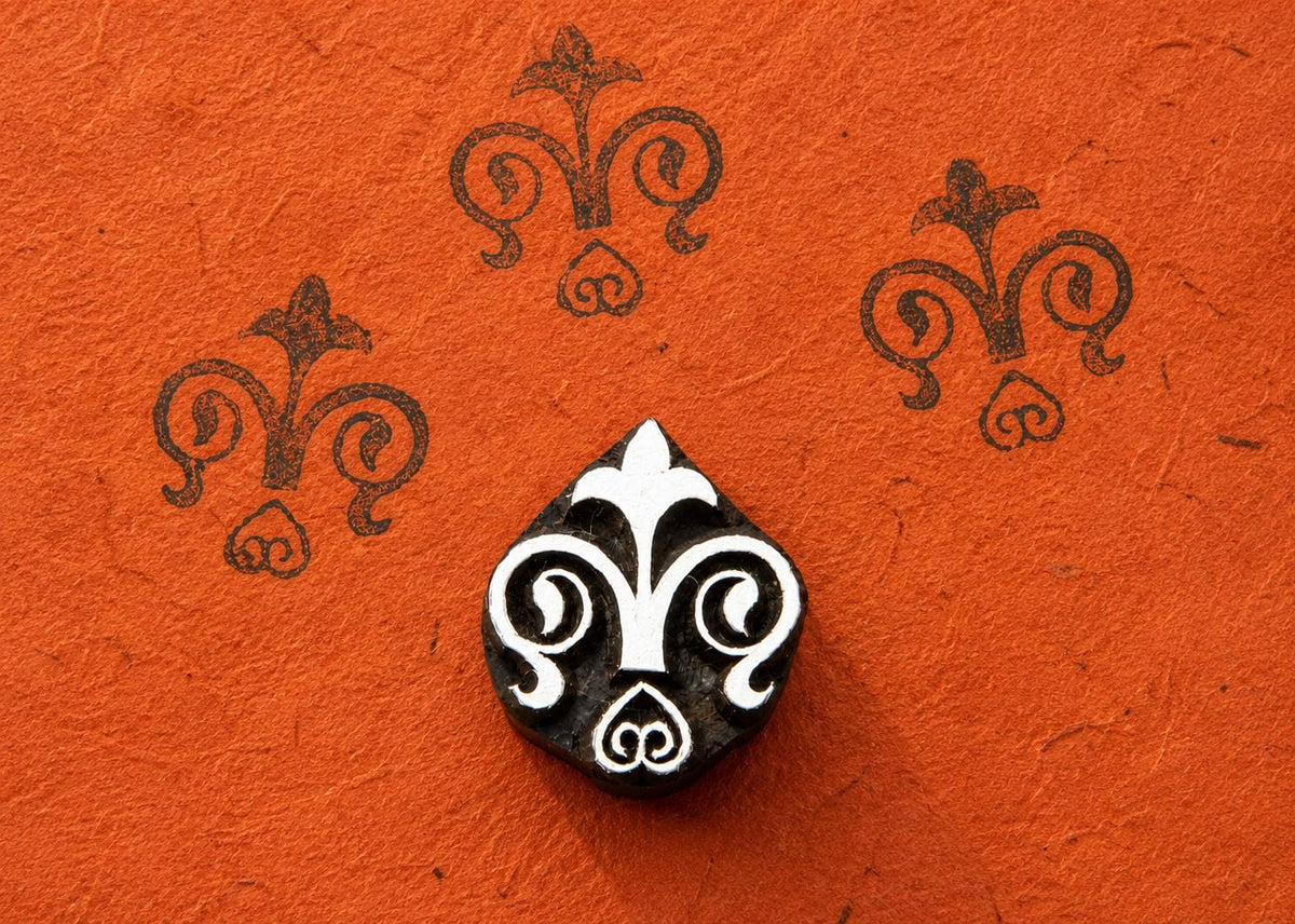 Small hand carved wooden floral motif block stamp printing repeating fleur inspired folk pattern on textured terracotta paper