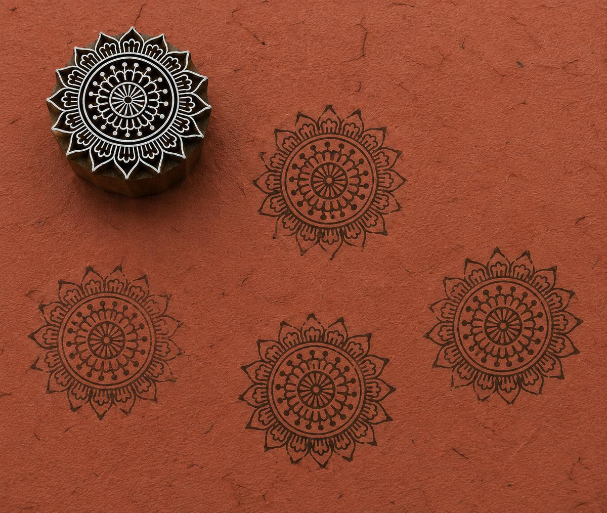 Hand-carved wooden printing block stamp featuring a temple mandala motif with layered ornamental details, shown stamped on textured terracotta handmade paper.