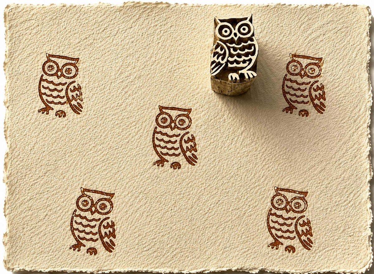 Hand carved owl block stamp creating repeated owl impressions on handmade paper.