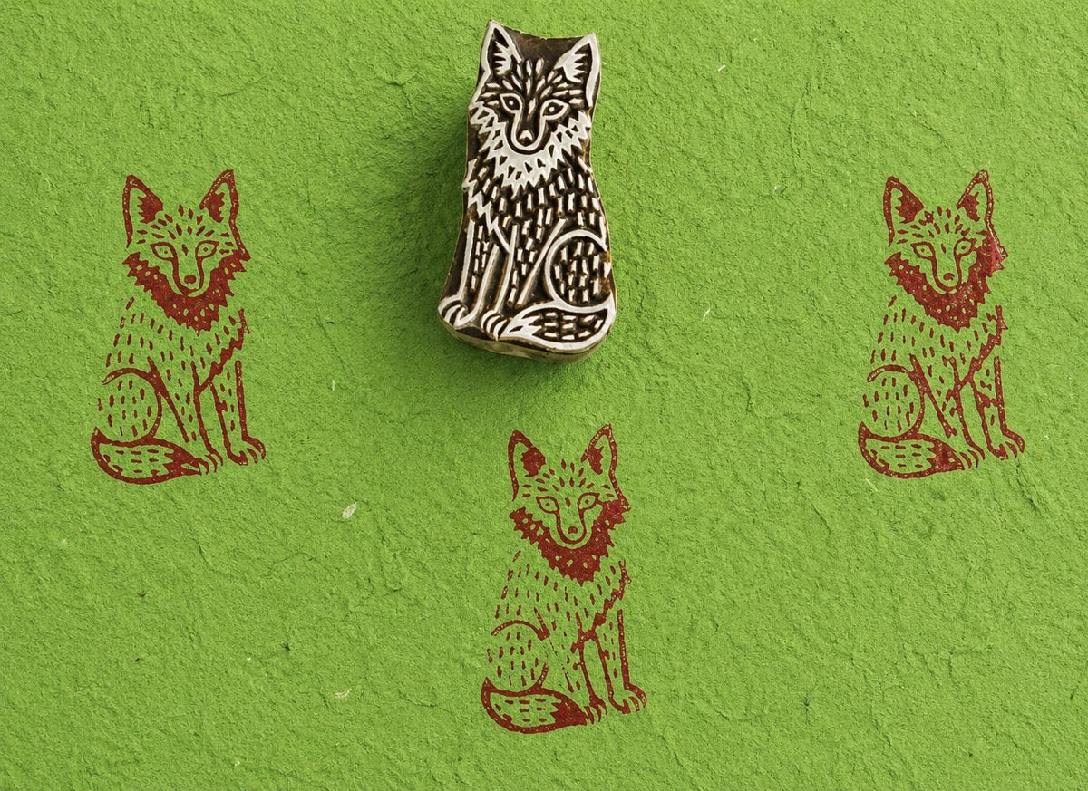 Hand carved wolf wooden printing block creating repeating rustic brown wolf prints on textured green handmade paper.