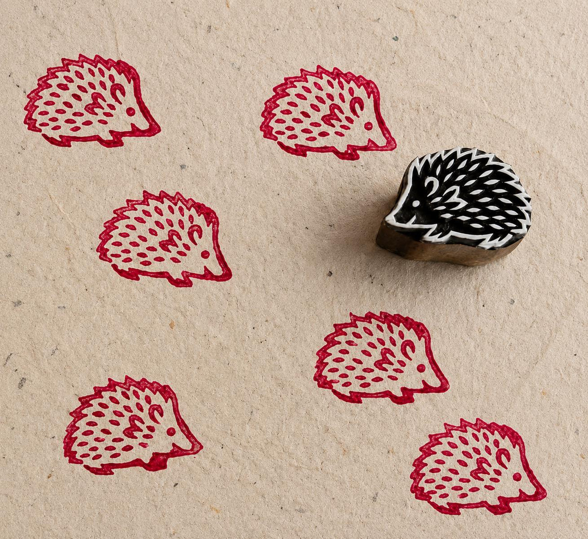 Hand carved hedgehog wood block stamp printing repeating folk animal patterns on textured paper