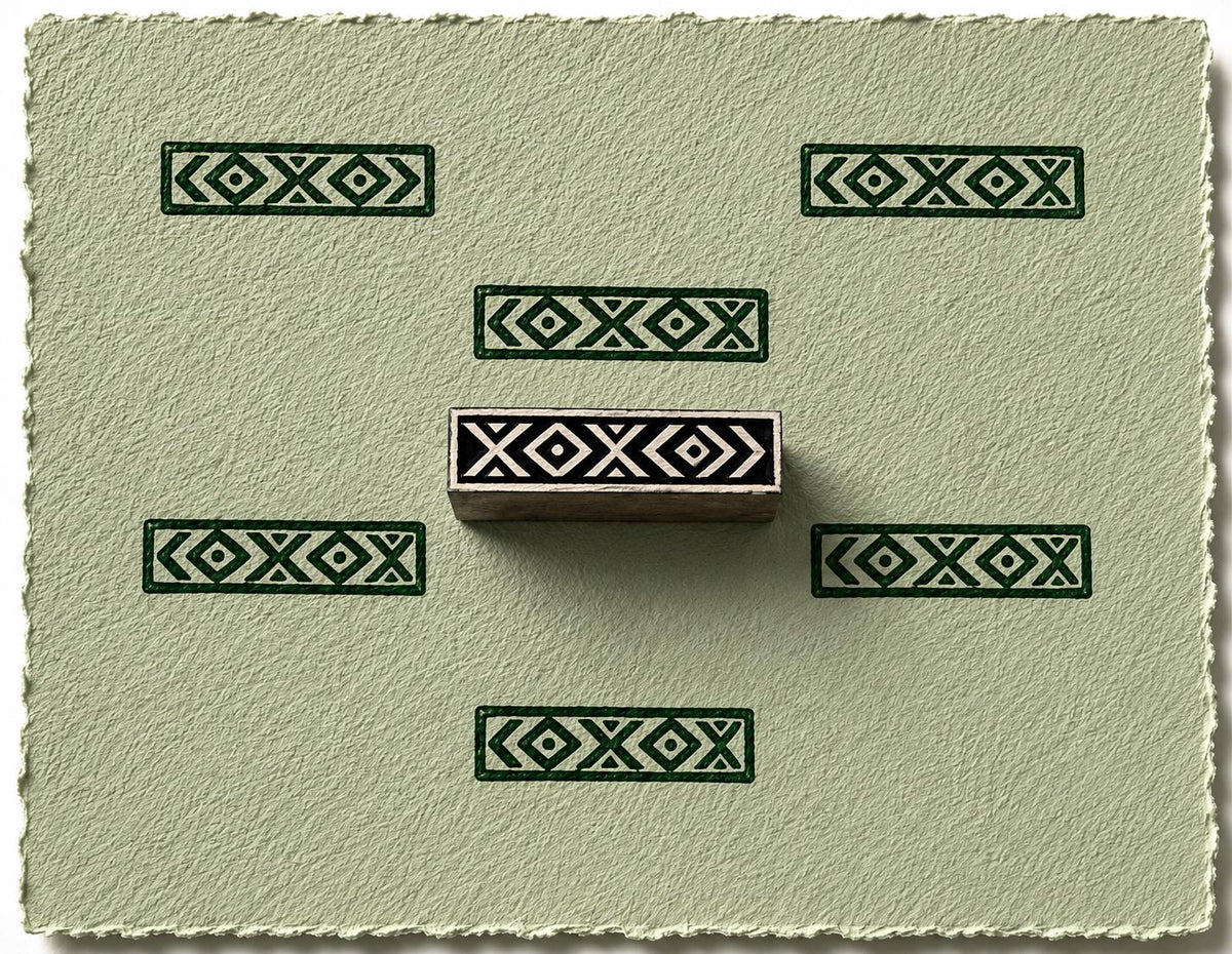 Hand carved wooden border printing block featuring a repeating diamond and chevron pattern stamped in green on textured handmade paper.
