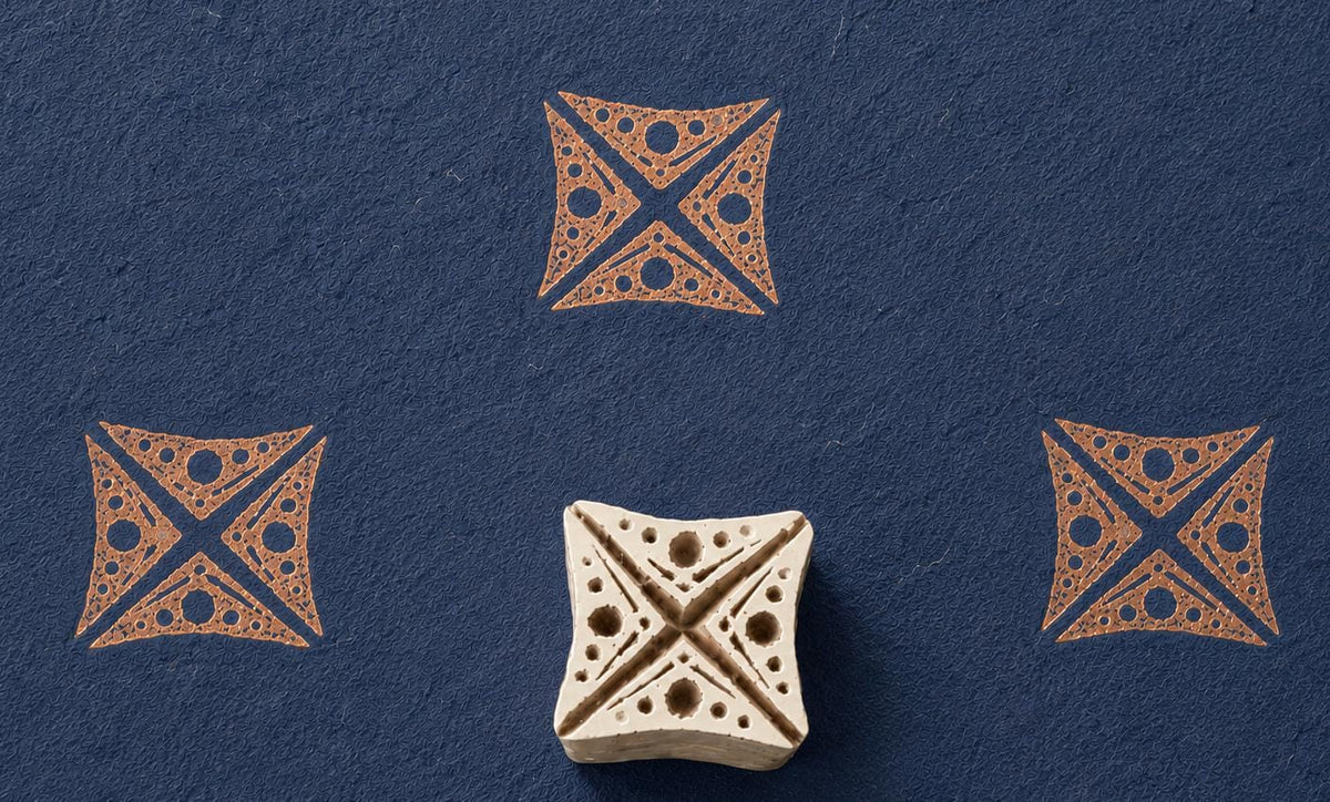 Hand-carved wooden printing block featuring a tribal geometric motif with dotted details, stamped in terracotta ink on textured navy handmade paper.