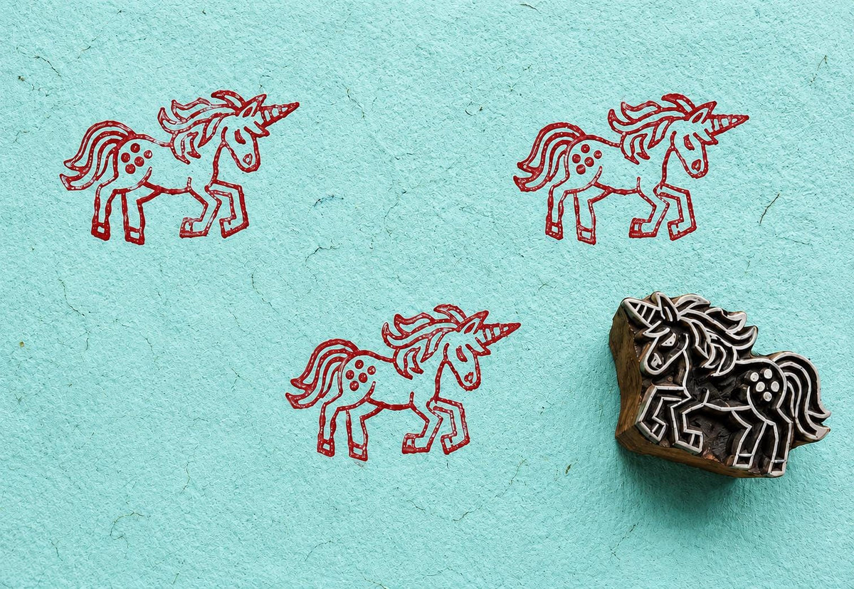 Hand carved wooden unicorn block stamp with red unicorn impressions on handmade turquoise paper.