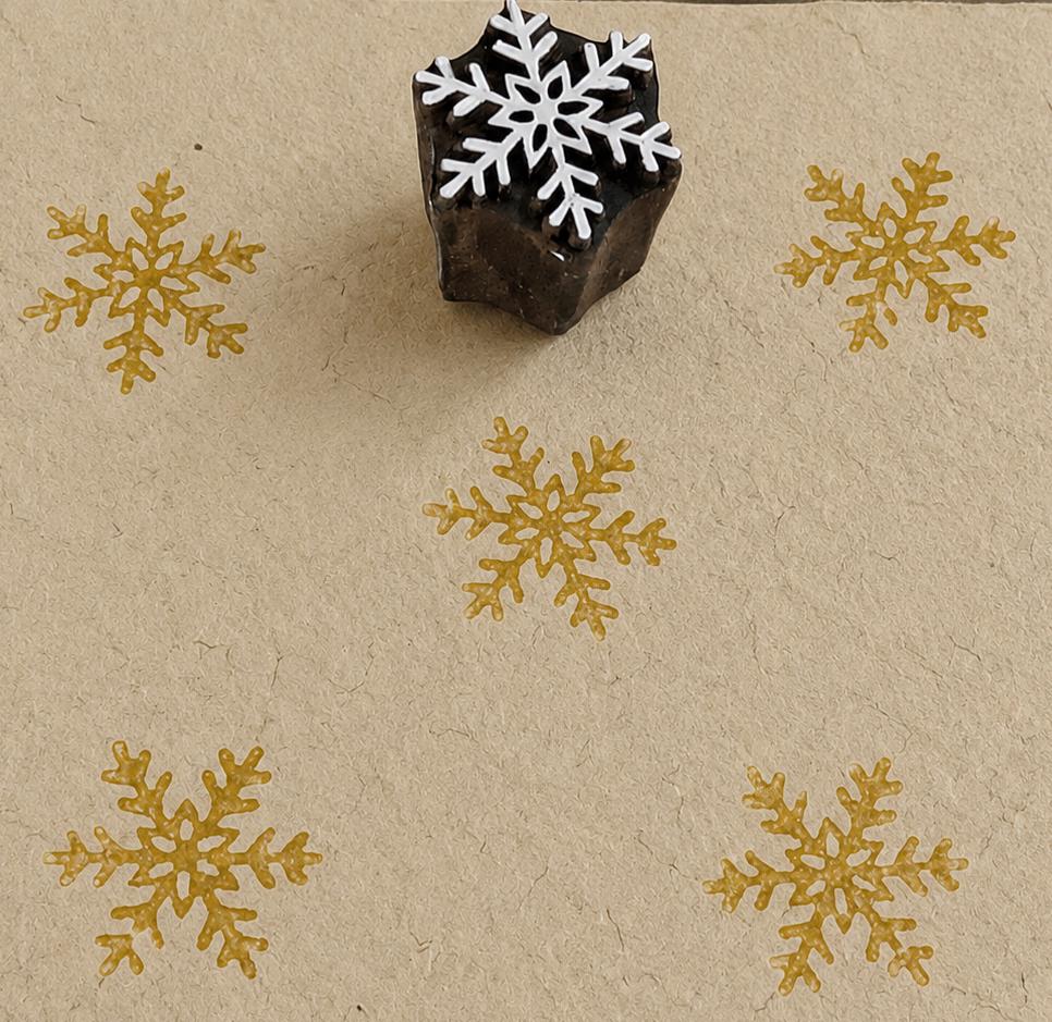 Hand carved snowflake wooden printing block with repeated golden snowflake impressions on handmade paper