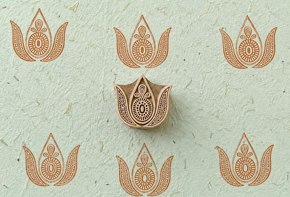 Hand-carved ornate paisley wooden printing block displayed on handmade paper with repeated decorative paisley impressions.