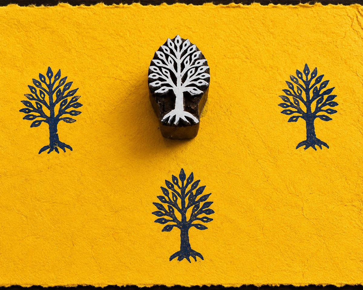 Hand carved Sacred Tree wooden block stamp with blue impressions on handmade yellow paper.