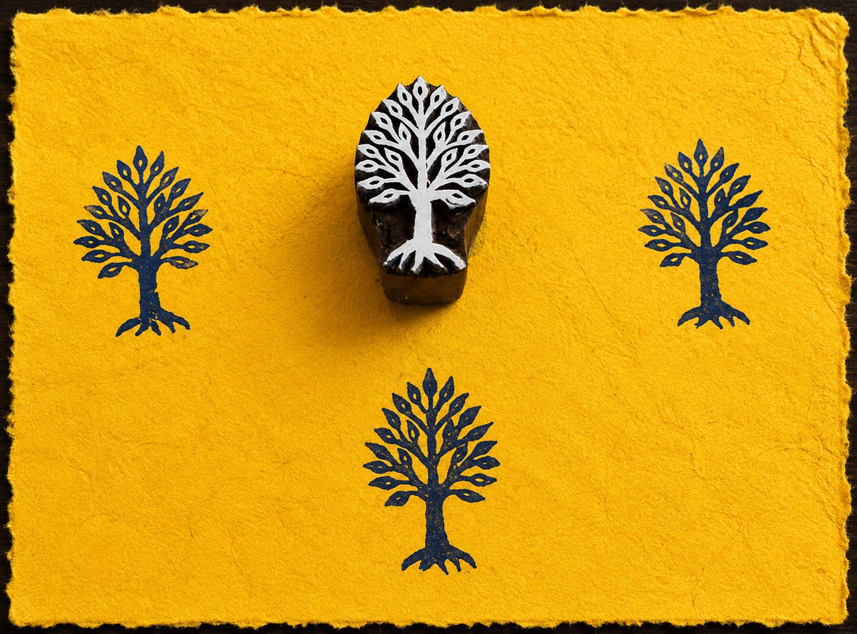 Hand carved Sacred Tree wooden block stamp with blue impressions on handmade yellow paper.