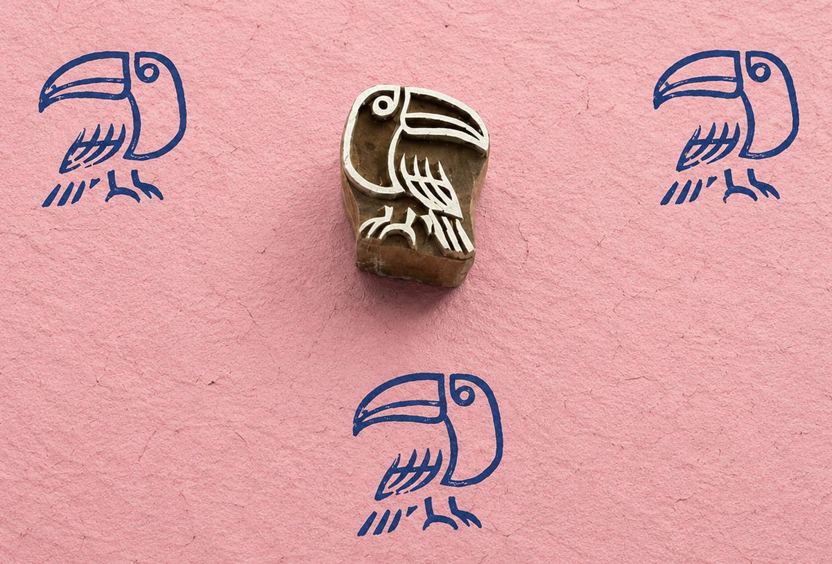 Hand carved folk art toucan block stamp with blue tropical bird impressions on pink handmade paper