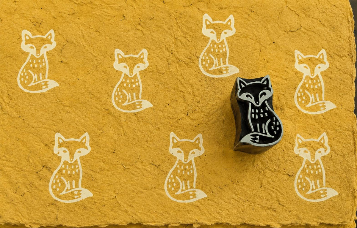 Hand-carved rustic fox wooden printing block with repeated fox prints on handmade yellow paper.