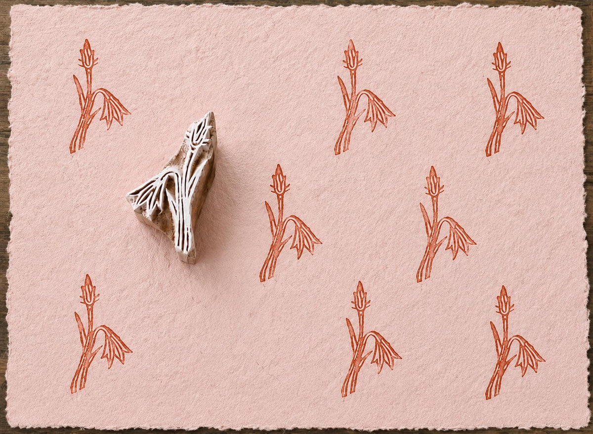 Hand carved snowdrop flower wooden block stamp displayed on pink handmade paper with repeating botanical impressions.