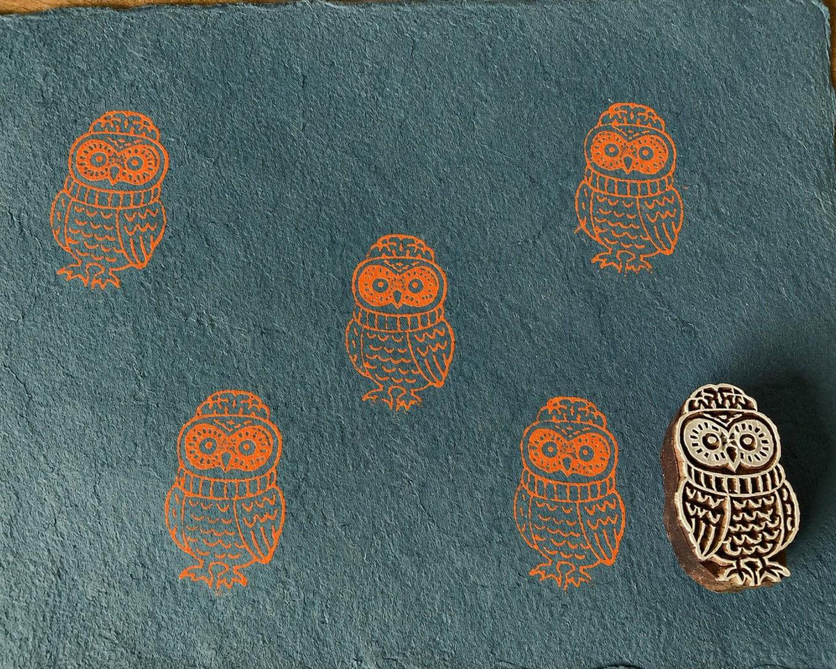 Hand-carved wooden cute owl printing block featuring an owl wearing a knitted hat, stamped in orange on teal handmade paper.