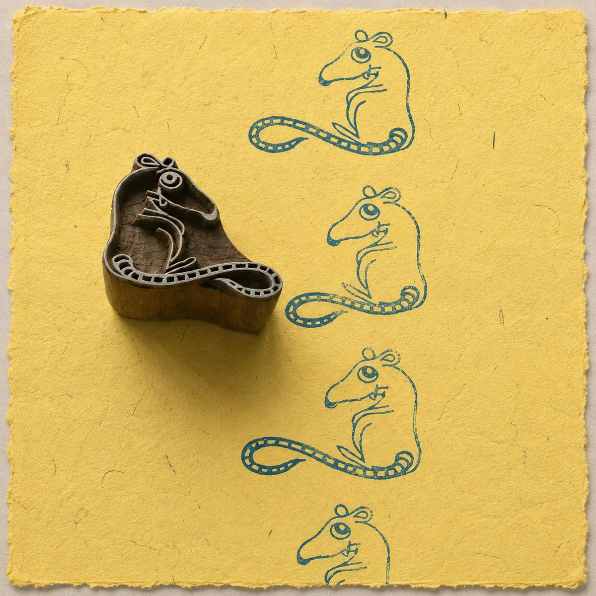 Hand-carved wooden mouse printing block with cute mouse impressions on yellow handmade paper, ideal for fabric printing, journaling, pottery, and paper crafts.