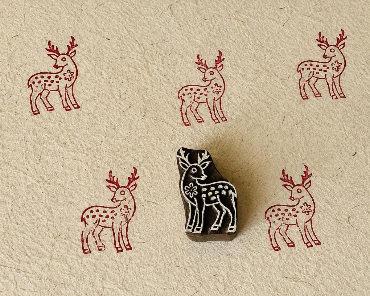 Hand-carved wooden floral deer printing block with repeated burgundy deer impressions on handmade paper.