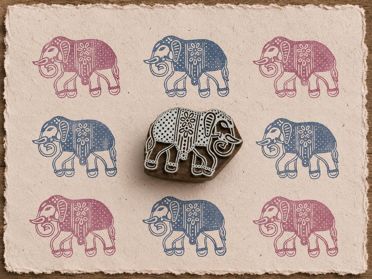 Hand-carved Indian elephant wooden printing block displayed with alternating blue and pink elephant impressions on textured handmade paper.