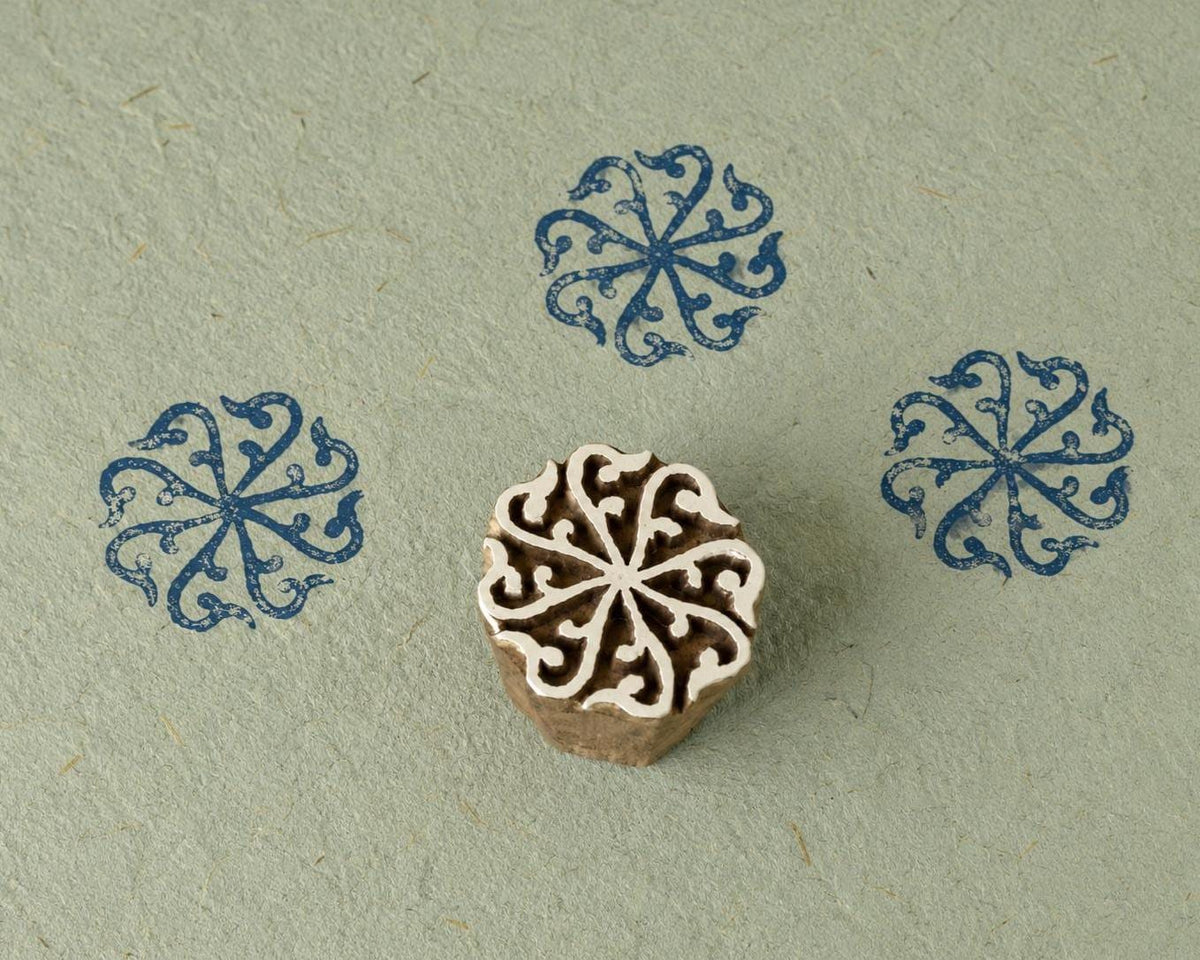 Hand carved wooden printing block featuring a circular scroll rosette motif with blue stamped impressions on handmade paper.