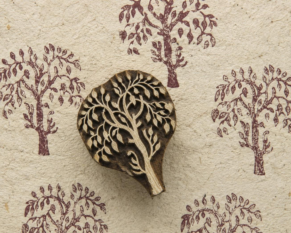 Hand carved wooden printing block featuring a twisted willow tree design stamped repeatedly on handmade textured paper in muted plum ink