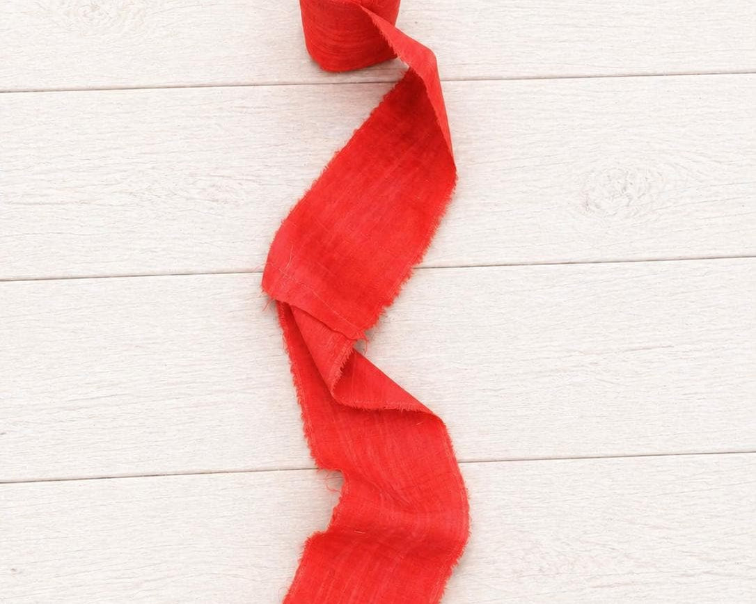 Single roll of extra wide vermilion sari silk ribbon unrolling to showcase its rich texture and frayed edges.