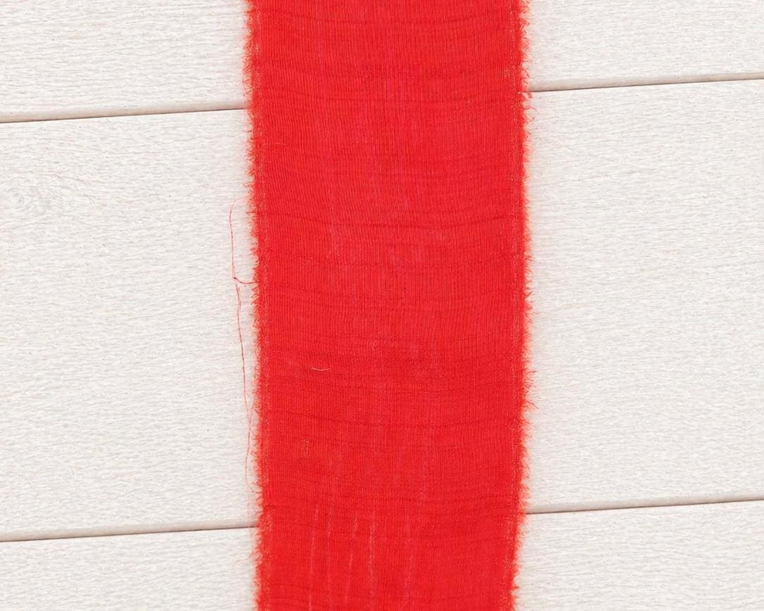 Flat section of wide vermilion sari silk ribbon displaying the smooth silk weave and generous width.