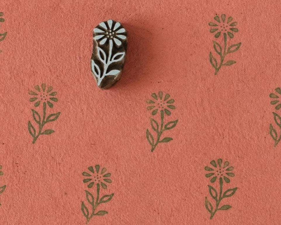 Hand-carved wooden floral printing block with repeated wild meadow flower impressions on coral handmade paper, perfect for fabric printing, stationery, and botanical crafts.