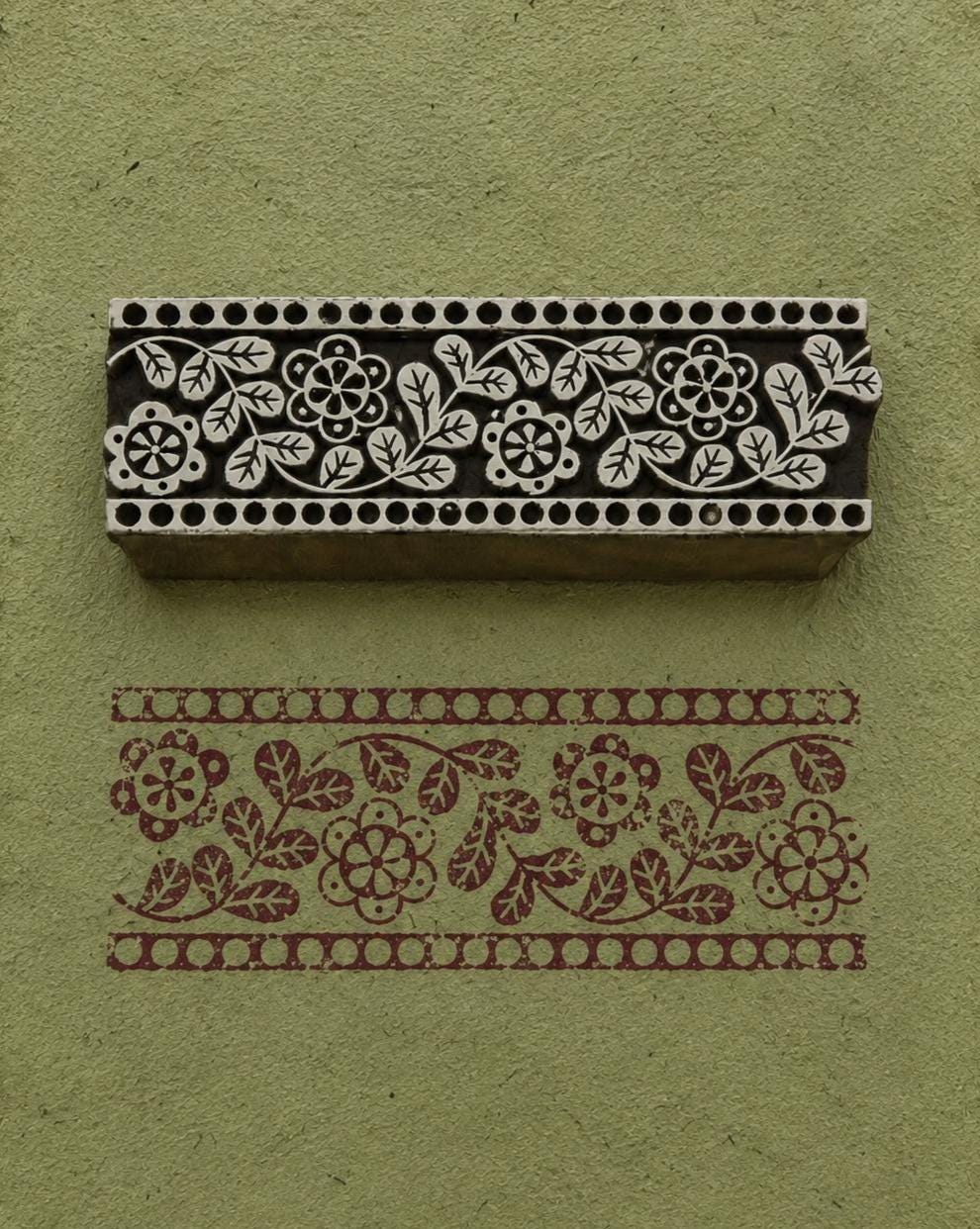 Hand-carved floral border wooden printing block with botanical border impressions on sage green handmade paper for fabric printing and paper crafts.