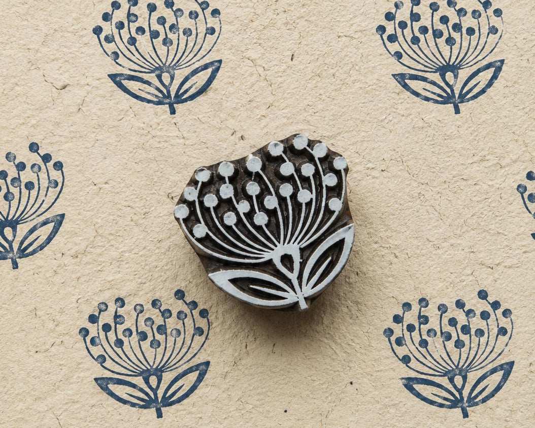Hand-carved dandelion flower wooden printing block surrounded by repeated navy blue botanical impressions on textured handmade paper.