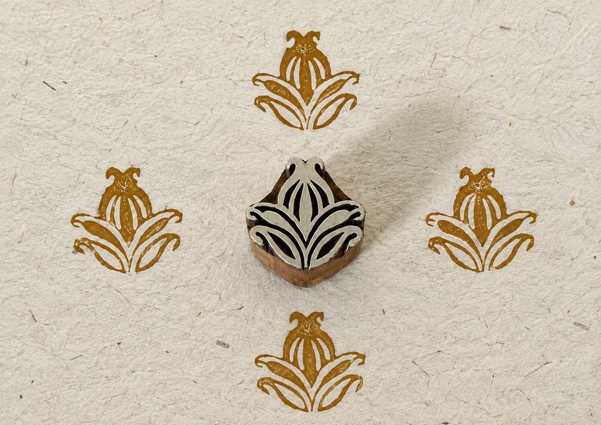 Hand carved Indian wooden textile printing block with a symmetrical stylised leaf and floral motif, shown with four ochre impressions on handmade paper.