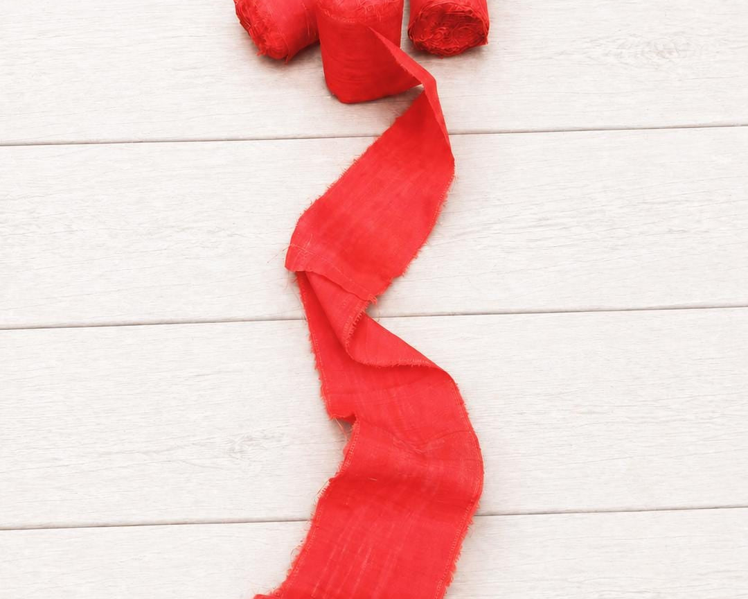 Extra wide vermilion recycled sari silk ribbon with three rolls and a flowing length displayed on a white wooden background.