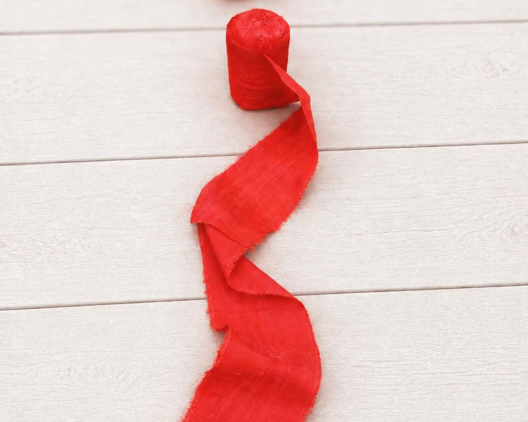 Single roll of vermilion wide recycled sari silk ribbon with softly blurred rolls in the background.