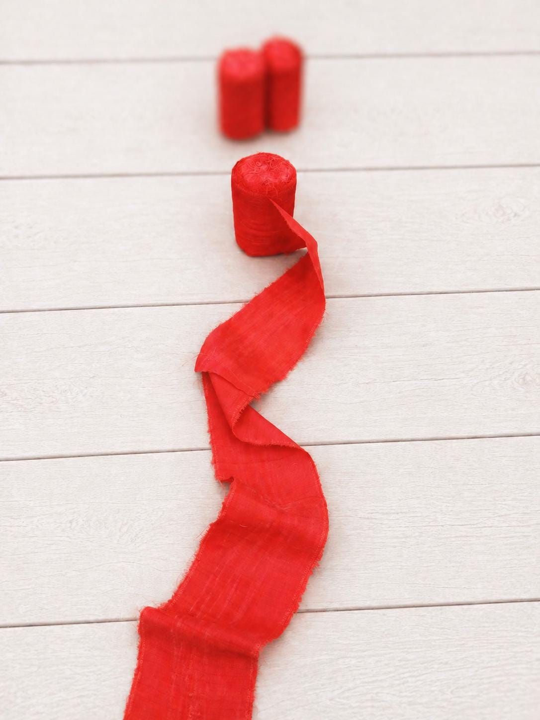 Single roll of vermilion wide recycled sari silk ribbon with softly blurred rolls in the background.