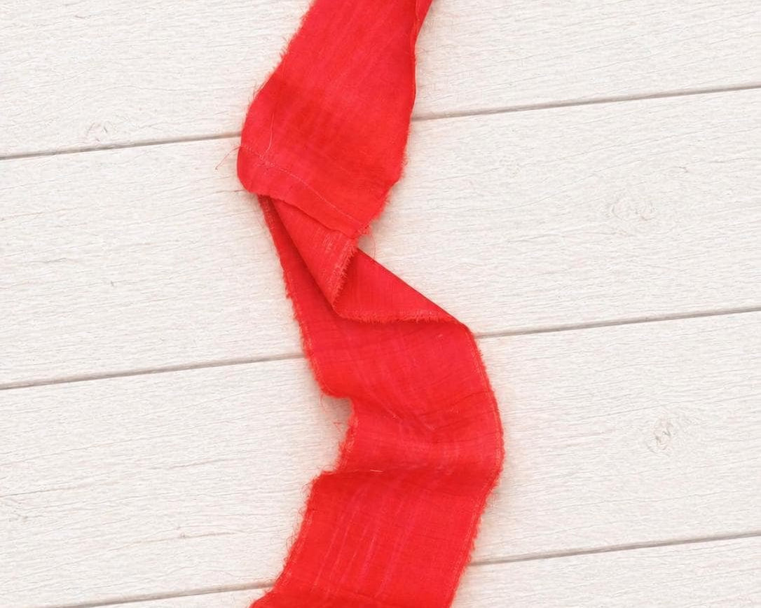 Close-up of wide vermilion recycled sari silk ribbon showing its soft drape, woven silk texture, and raw frayed edges.