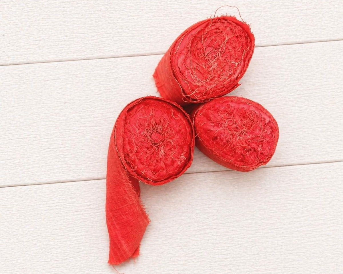 Top view of three rolled bundles of extra wide vermilion recycled sari silk ribbon.