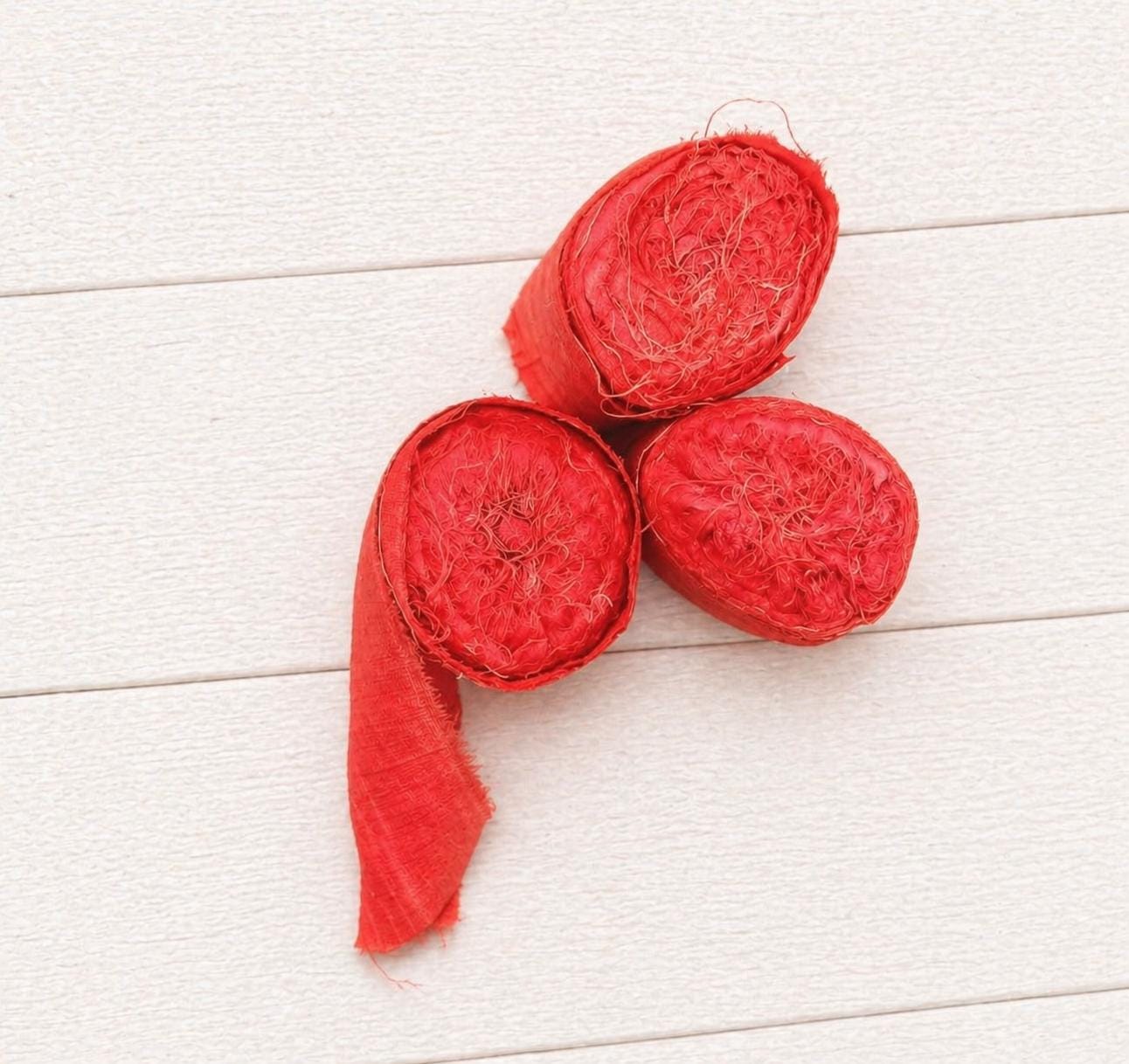 Top view of three rolled bundles of extra wide vermilion recycled sari silk ribbon.