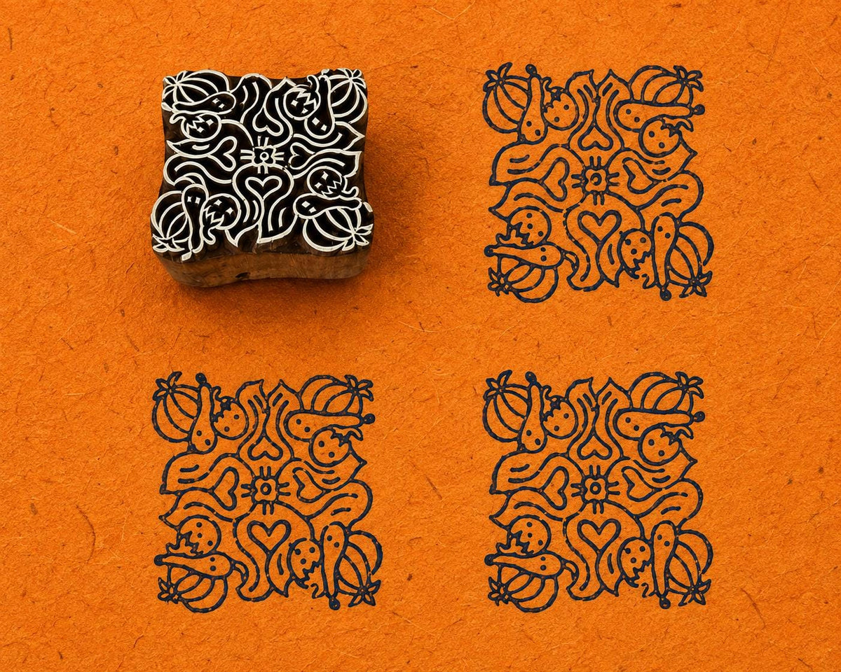 Hand carved wooden printing block with a dense folk floral motif of flowers, curling leaves, fruit-like forms and a central heart, shown with three blue impressions on textured orange handmade paper.