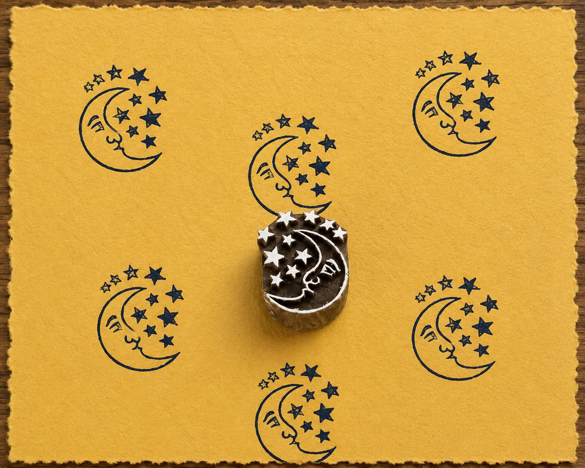 Hand-carved Starlit Moon wooden printing block with navy blue moon and stars impressions on mustard handmade paper.