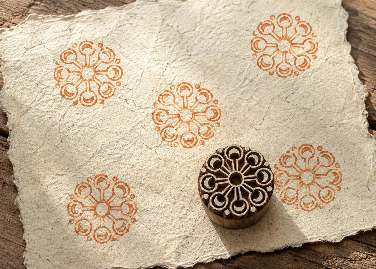 Hand-carved Crescent Sunwheel wood block stamp with warm terracotta circular medallion impressions on textured handmade paper.