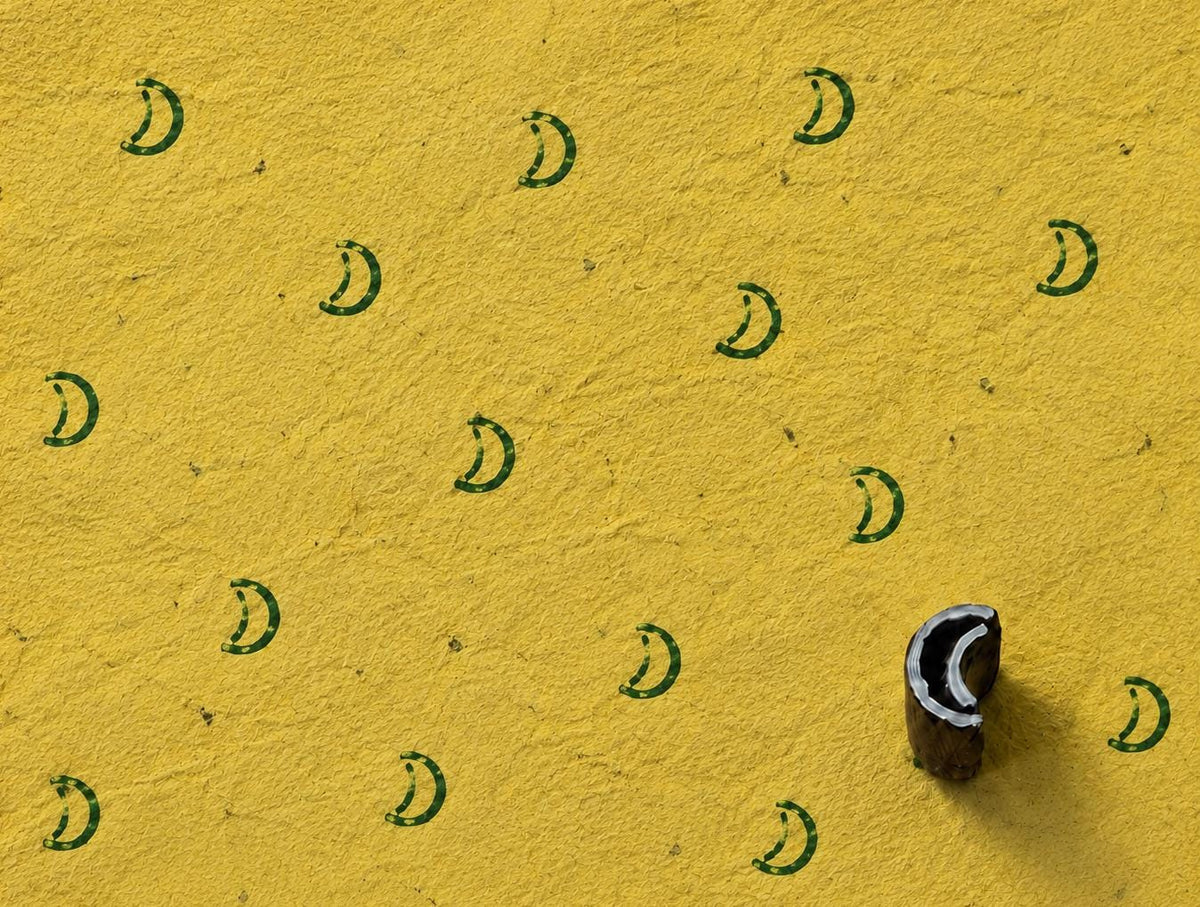 Tiny hand carved wooden crescent moon printing block measuring approximately 1.6 × 1.2 cm, shown with repeated green crescent impressions on textured handmade yellow paper.